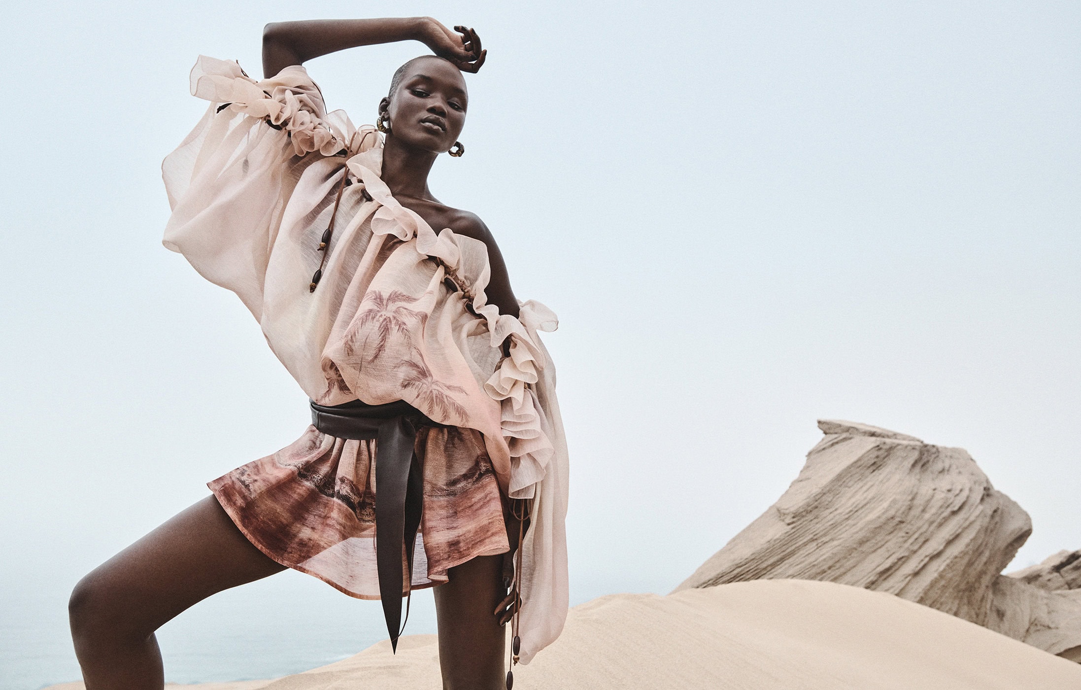 Model Abeeny Nhial wearing a ruffled top and printed mini dress posed on a sand dune in Morocco