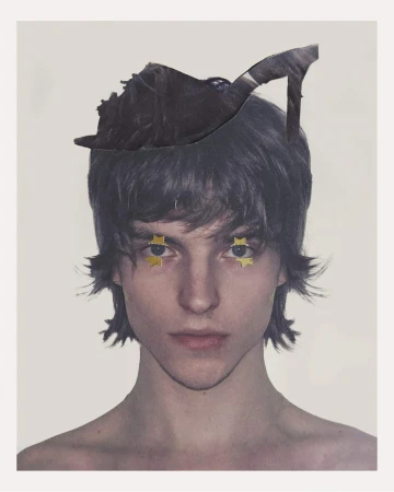 Portrait of a person with dark shaggy hair, small gold star eye decorations, and a cut-out high-heeled shoe resting on their head.