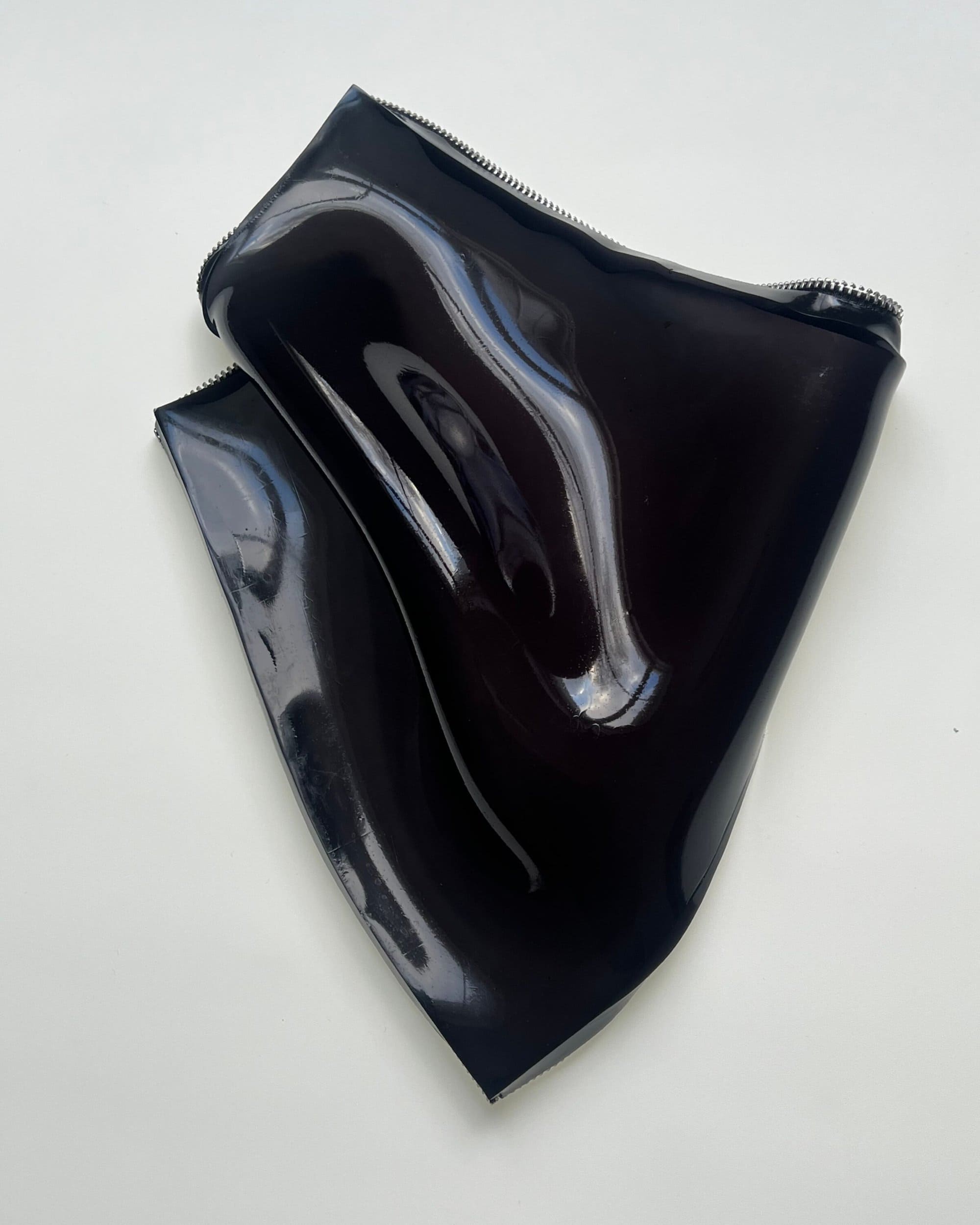 Glossy black patent leather accessory with visible zippers against a plain light background for Paul Andrew.