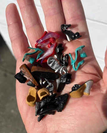 An open human palm holding a collection of miniature high-heeled doll shoes in various colors and styles.