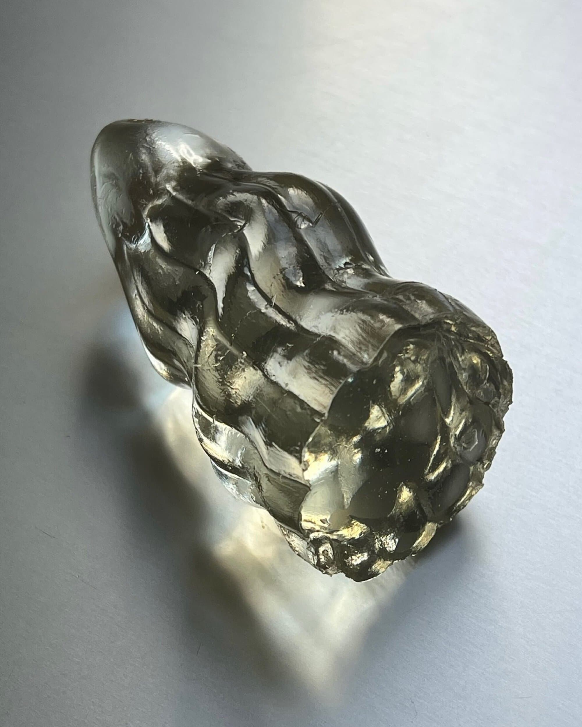 Close-up of a translucent ribbed glass sculpture piece resting on a reflective white gradient background surface.
