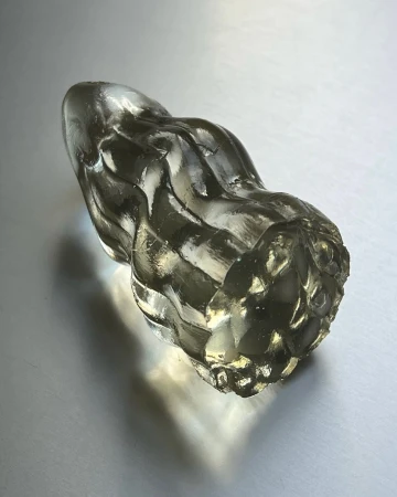 Close-up of a translucent ribbed glass sculpture piece resting on a reflective white gradient background surface.