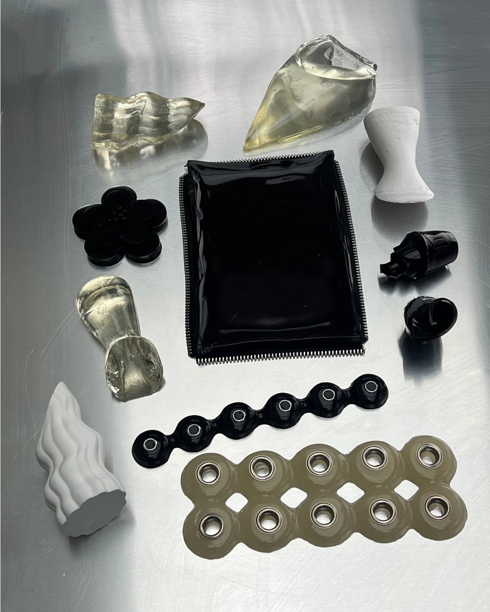Flat lay of small sculptural objects, hardware components, and geometric shapes arranged on a metallic brushed surface.