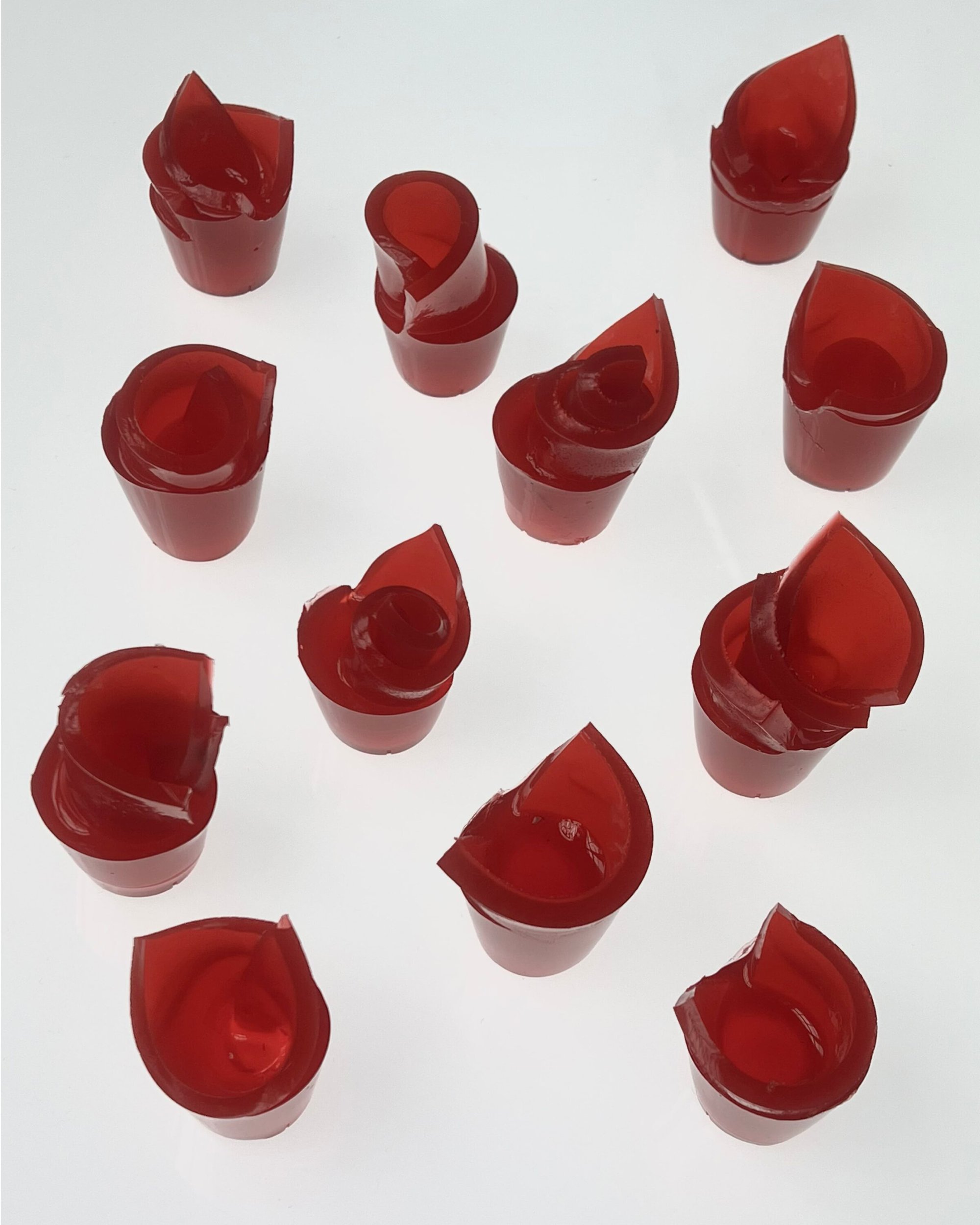 An arrangement of translucent red gelatin shapes in small cups on a seamless white background.