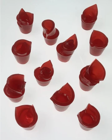 An arrangement of translucent red gelatin shapes in small cups on a seamless white background.
