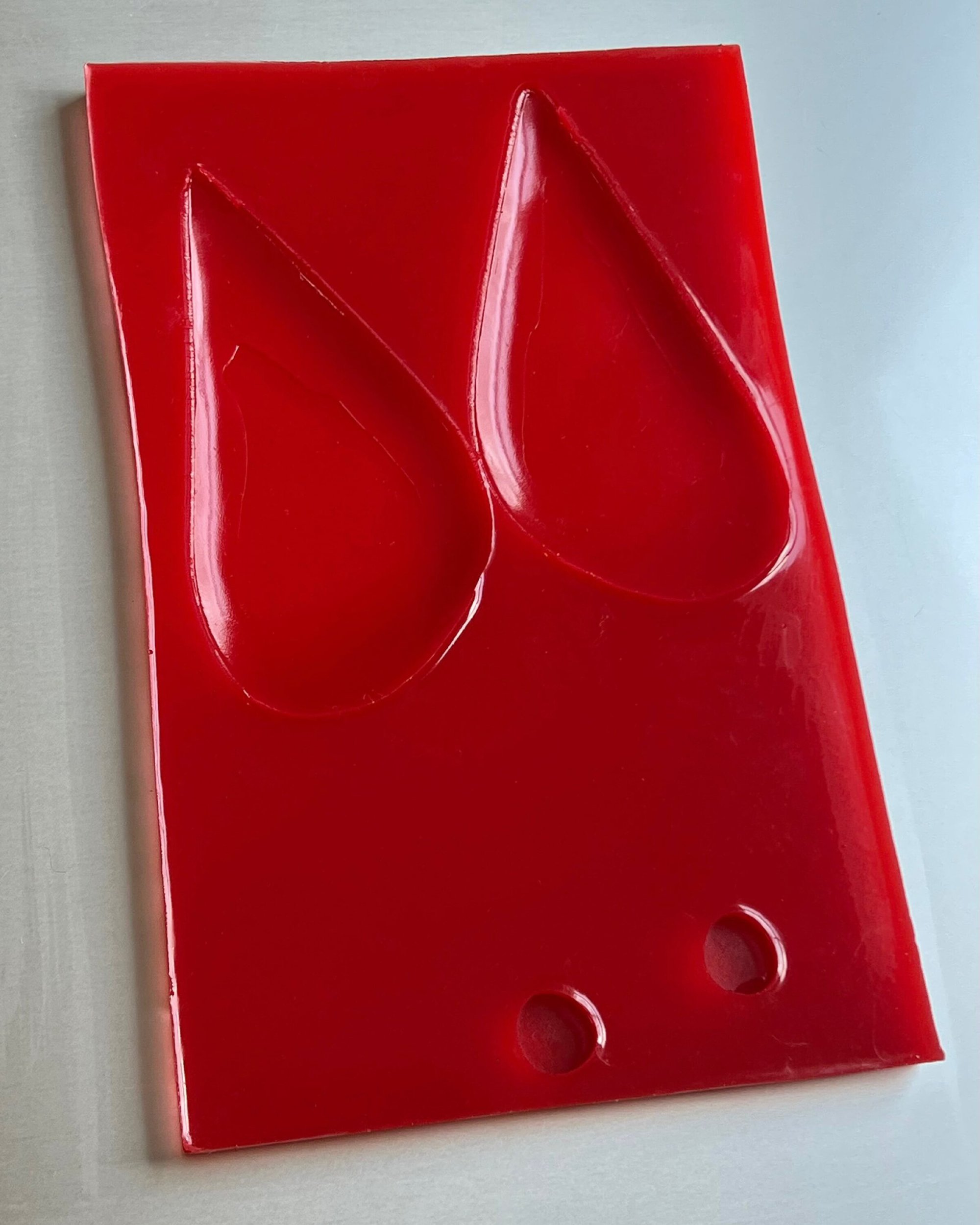 Glossy red acrylic plaque featuring two recessed teardrop shapes and two small circular holes at the base