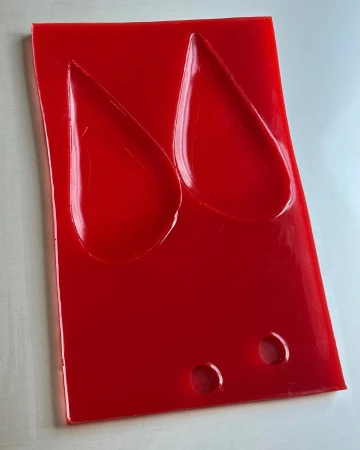 Glossy red acrylic plaque featuring two recessed teardrop shapes and two small circular holes at the base