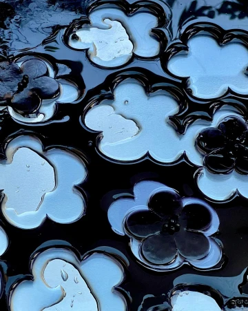 Close-up abstract shot of glossy flower-shaped cutouts revealing blue and dark liquid surfaces with water droplets