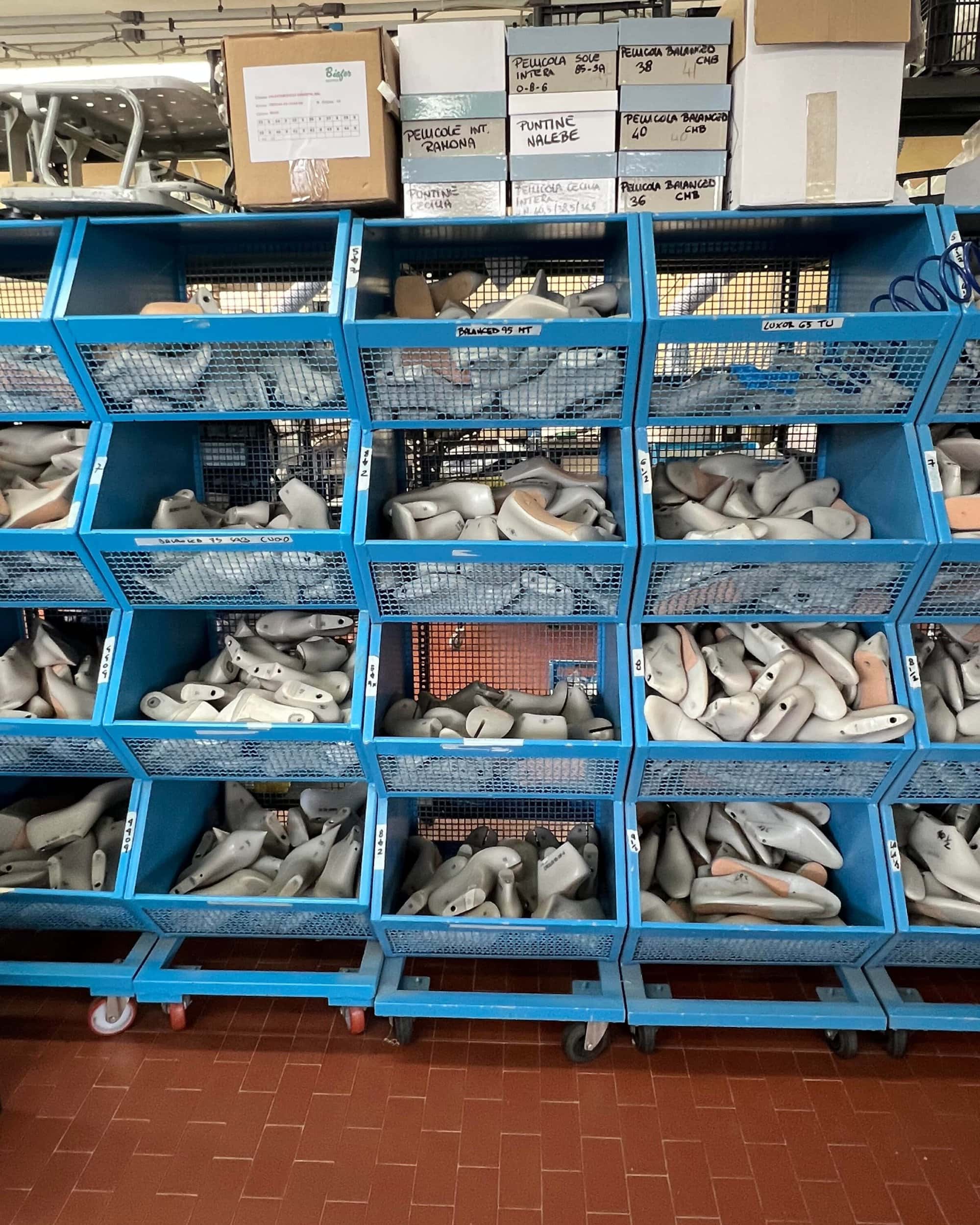 Blue wire storage bins filled with shoe lasts on shelves inside a manufacturing workshop