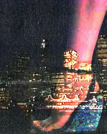 Close-up of a person's leg and foot wearing a heeled shoe against a nighttime cityscape background with grainy texture
