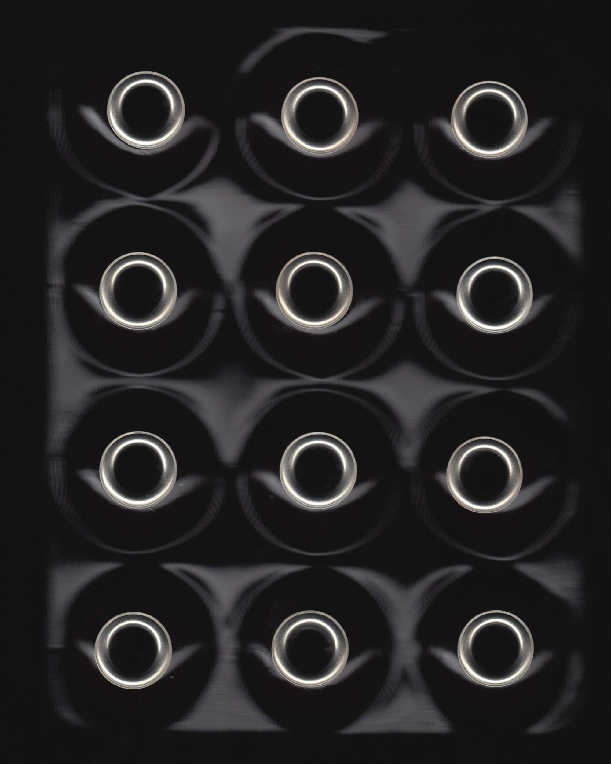 Overhead view of twelve metallic circular rings arranged in a grid pattern against a dark background.