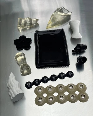 Flat lay of small sculptural objects, hardware components, and geometric shapes arranged on a metallic brushed surface.