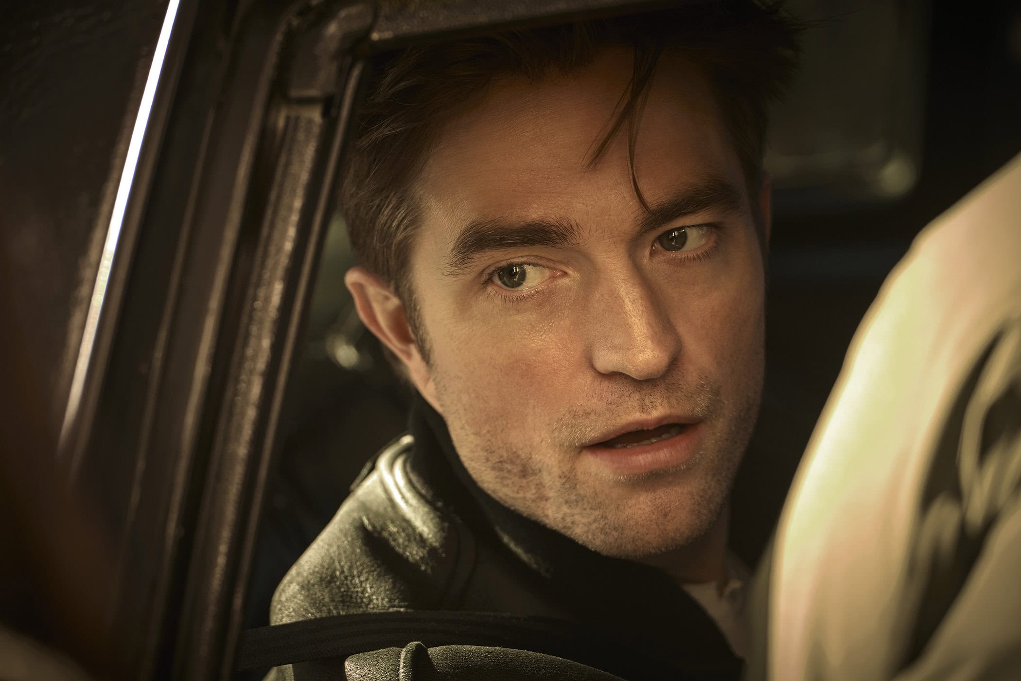 Close-up portrait of Robert Pattinson looking out from inside a vehicle window for a Dior fragrance advertising campaign.