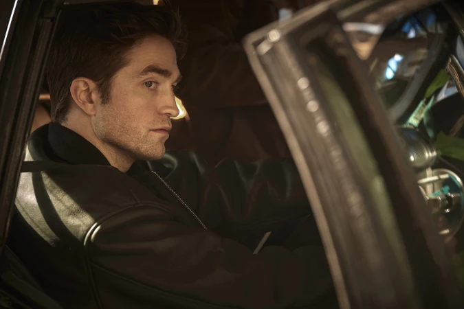 Robert Pattinson seated inside a car wearing a dark jacket for the Dior Homme Parfum advertising campaign.