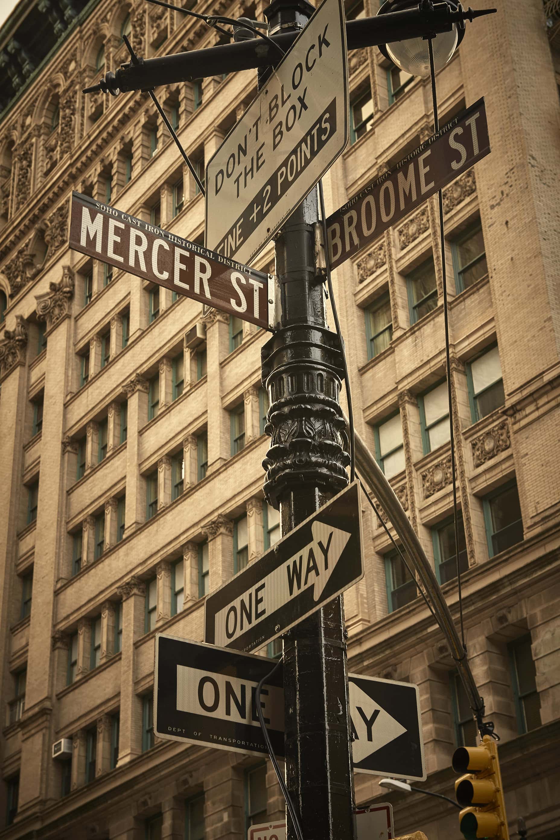 Mercer St and Broome St street sign post against a classic New York City commercial building exterior in sepia tones.