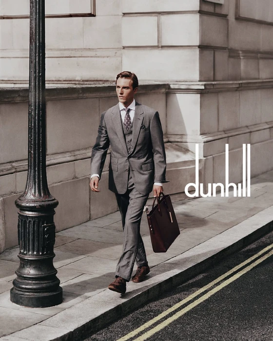 A man in a grey suit holding a leather briefcase walking past a lamppost on a city street for Dunhill.