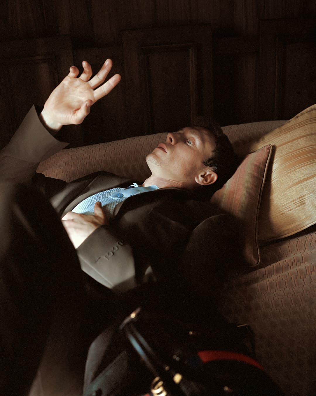 Man wearing a dark suit lying on a bed with his hand raised in a Gucci spring ad campaign photograph