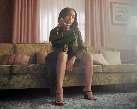 Yara Shahidi seated on a vintage sofa holding a green handbag for the Gucci Spring 2025 campaign.