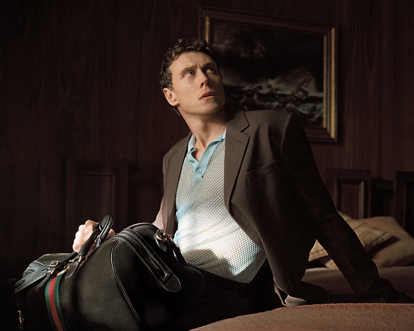 George MacKay holding a black travel bag in a hotel room for the Gucci Spring 2025 ad campaign.