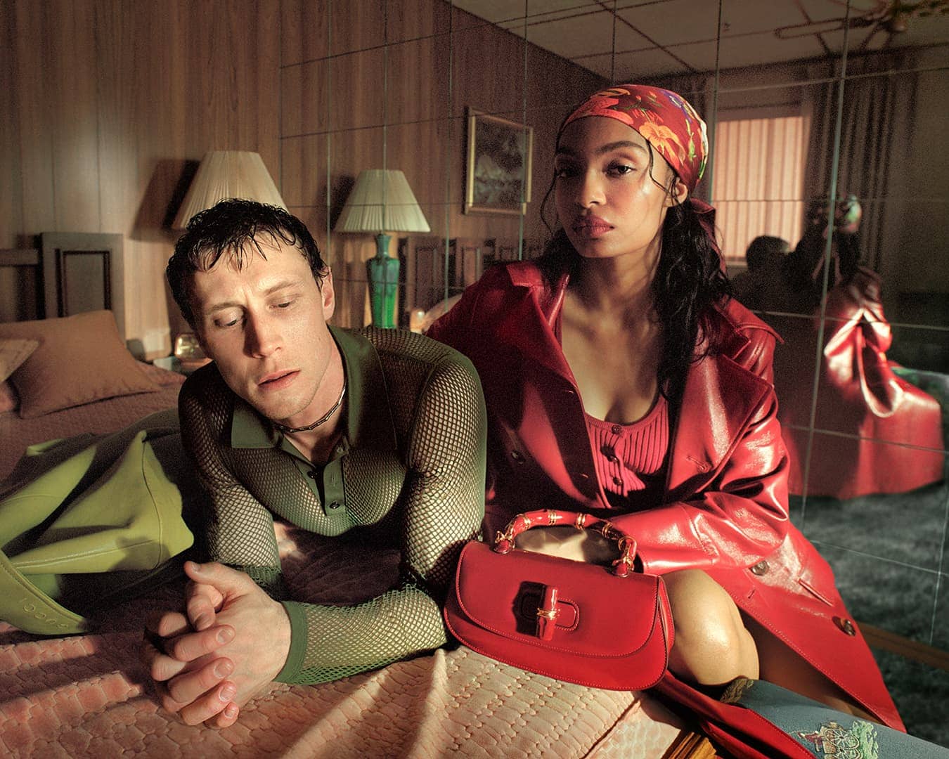 Yara Shahidi and George MacKay pose on a hotel bed for the Gucci Spring 2025 ad campaign, styled in vibrant red leather and olive mesh.