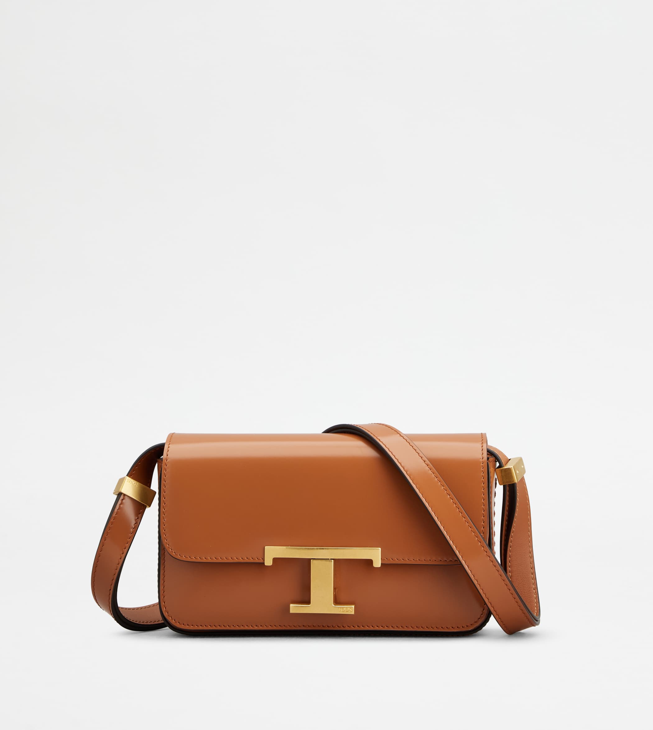 Tan leather shoulder bag with gold T clasp centered against a bright white studio background.