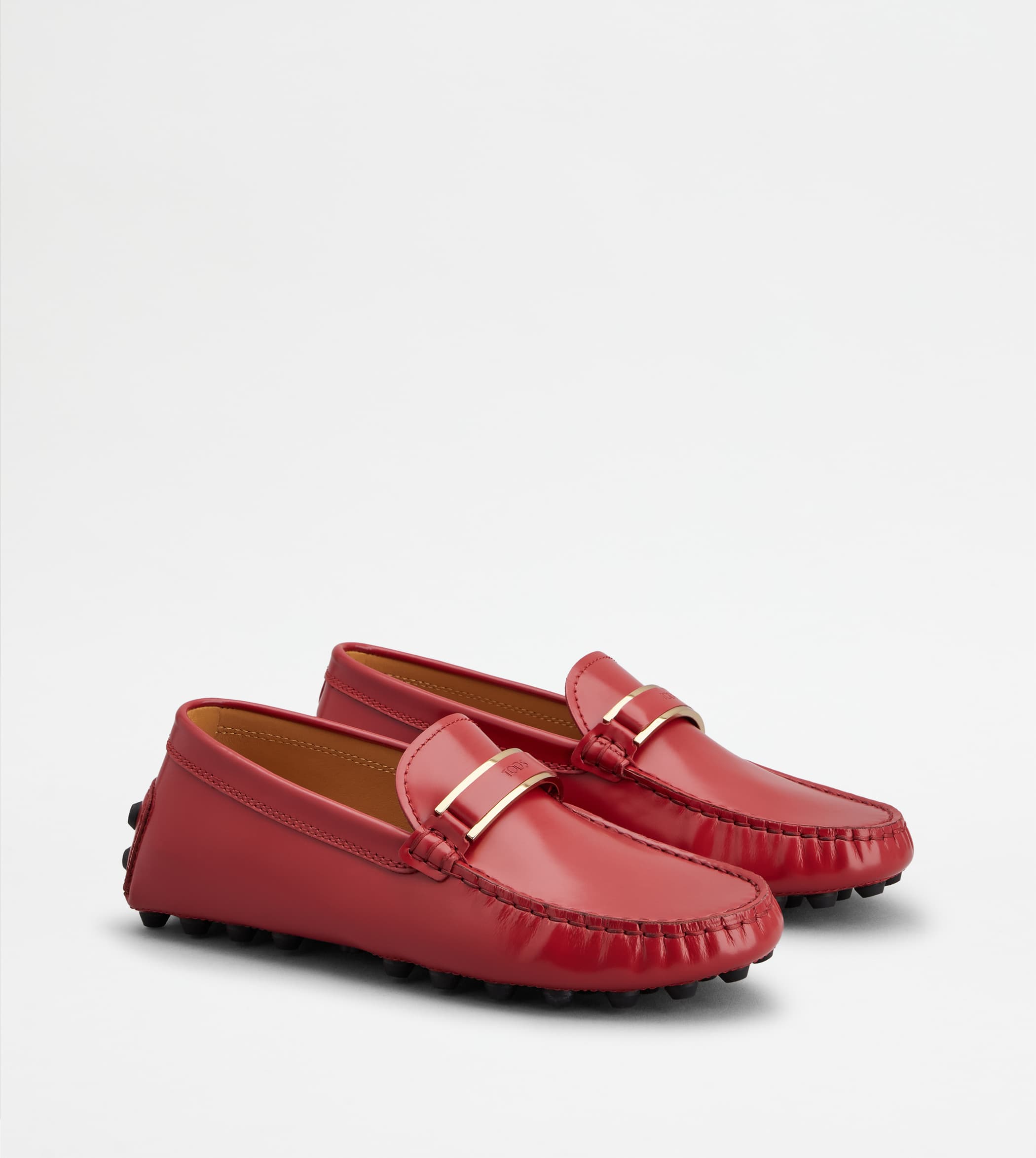 Pair of red leather loafers with gold hardware and pebble soles on a white background