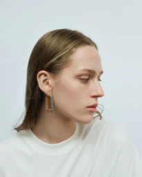 Close-up portrait of a woman wearing sculptural metallic earrings and a white t-shirt against a plain grey seamless background