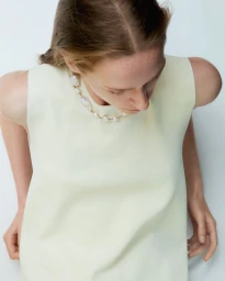 Model wearing a pale yellow sleeveless top and pearl necklace from above against a white background