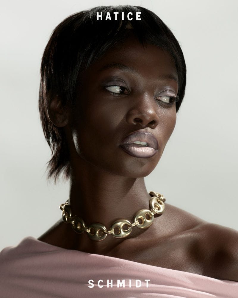 Portrait of a black woman wearing a gold link necklace and pink top against a light grey seamless background