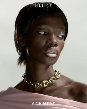 Portrait of a black woman wearing a gold link necklace and pink top against a light grey seamless background
