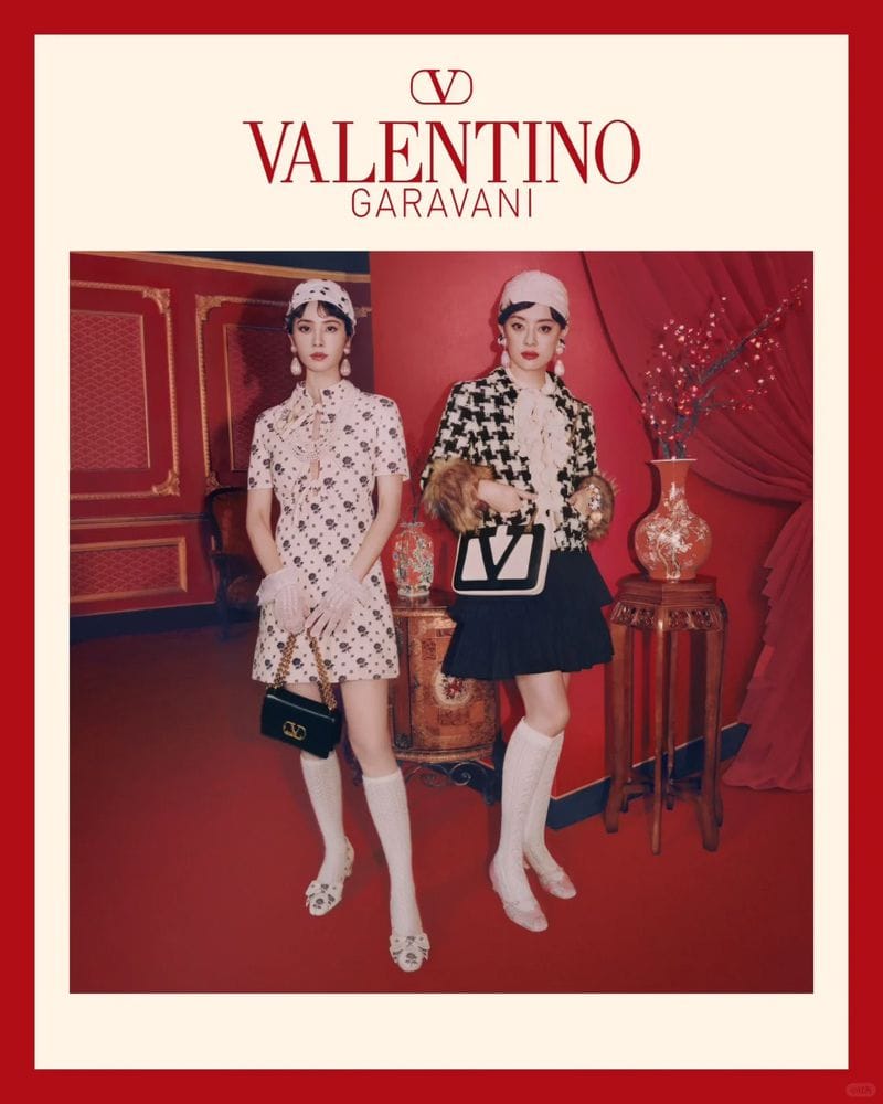 Two models wearing coordinated outfits and hats pose in a red-toned interior for a Valentino Lunar New Year campaign.