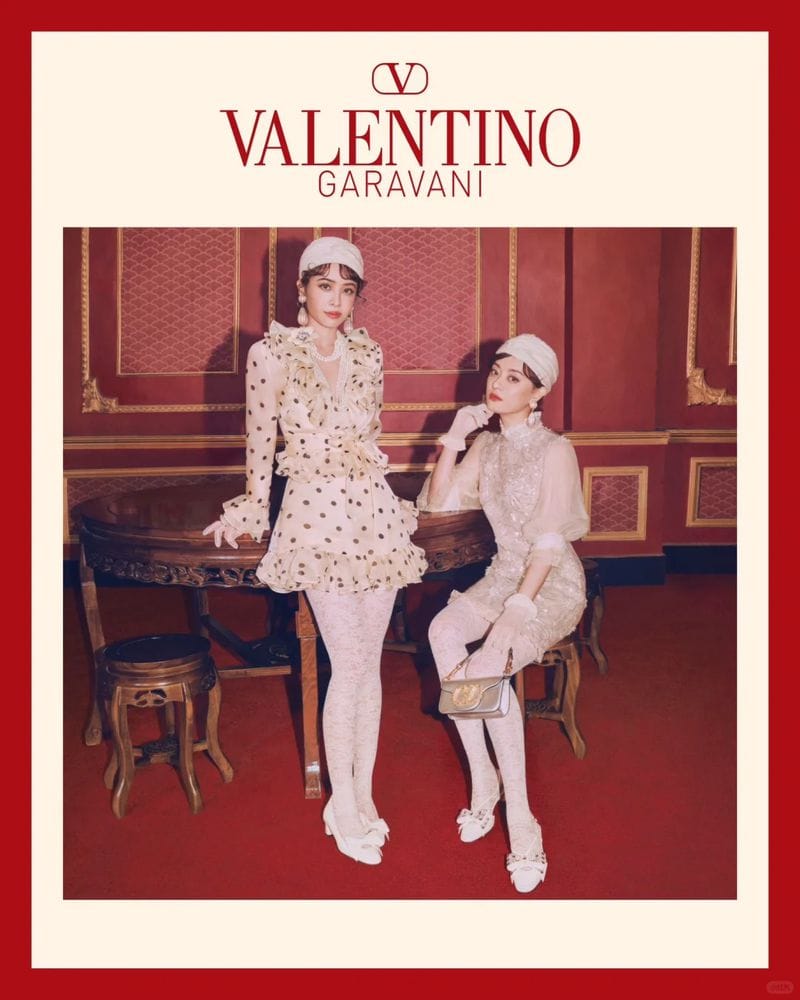 Two women in coordinated cream and patterned outfits posing in an interior room with red walls for Valentino Lunar New Year campaign.