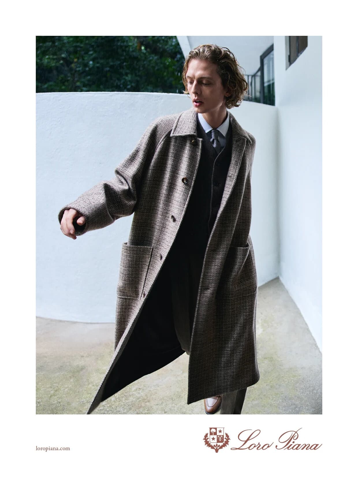 Model Leon Dame in a brown patterned coat for Loro Piana Spring 2025 ad campaign against a white architectural backdrop