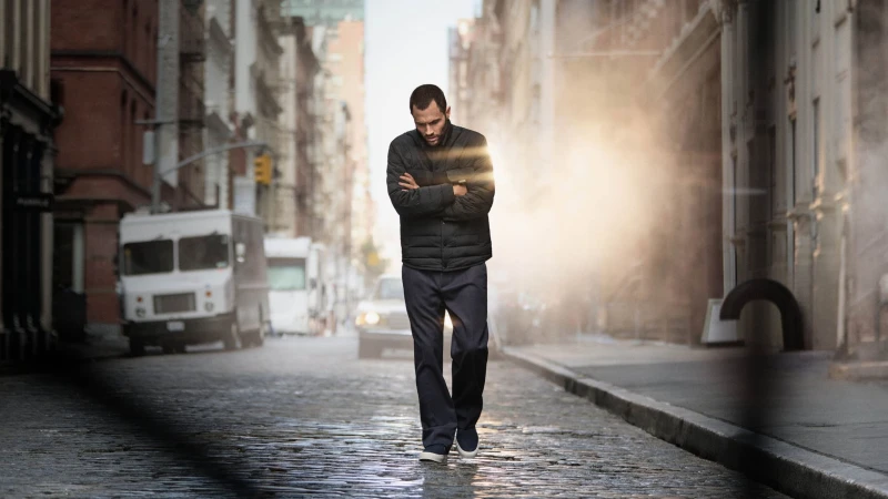 Penn Badgley walking on a New York City cobblestone street wearing a quilted black puffer jacket for Moncler.