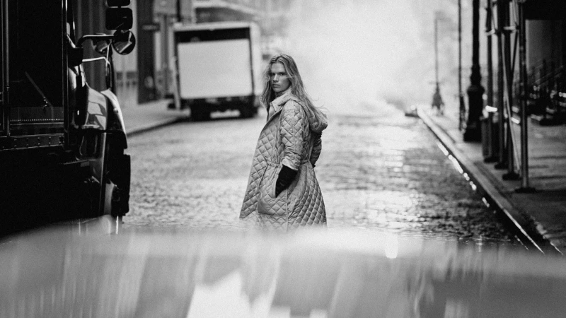 Monochromatic fashion editorial image featuring a model wearing a quilted coat walking down a city street