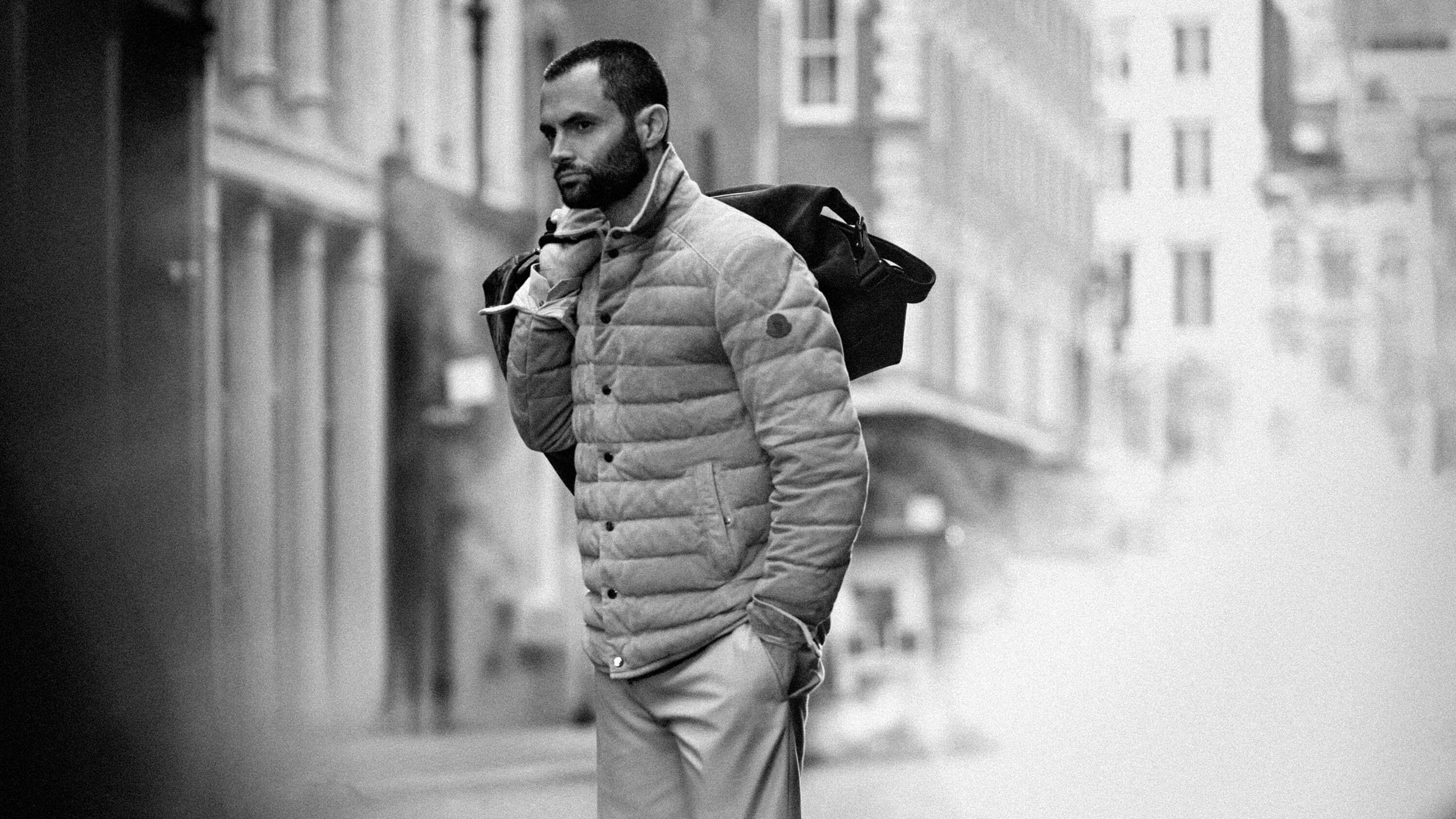 Moncler spring 2025 campaign image featuring Penn Badgley in a quilted jacket walking outdoors on a city street.