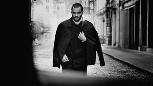 Penn Badgley walking on a city street wearing a dark jacket for the Moncler Spring 2025 campaign.