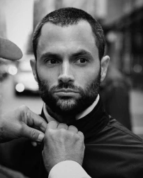 Close-up black and white portrait of Penn Badgley getting his jacket collar adjusted for Moncler.