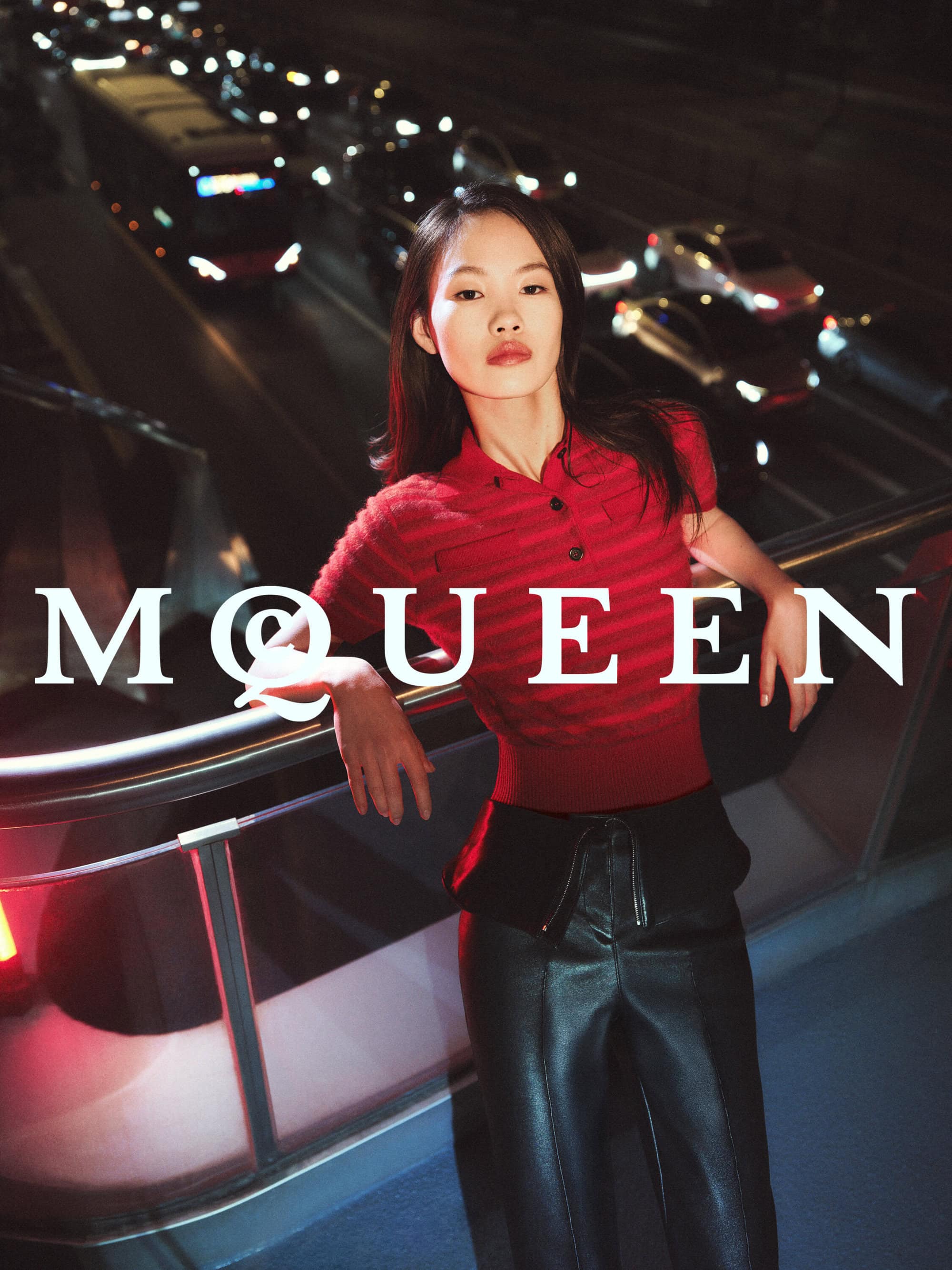 Model Zhang Youhao in a red polo top and black trousers leaning against an elevated walkway overlooking nighttime traffic.