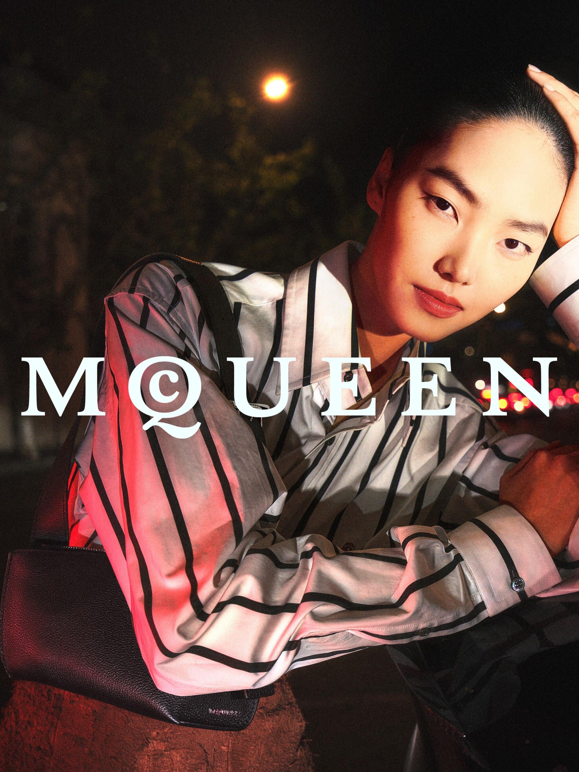 Model Zhang Youhao in a striped shirt posing for the McQueen Lunar New Year ad campaign under night city lights