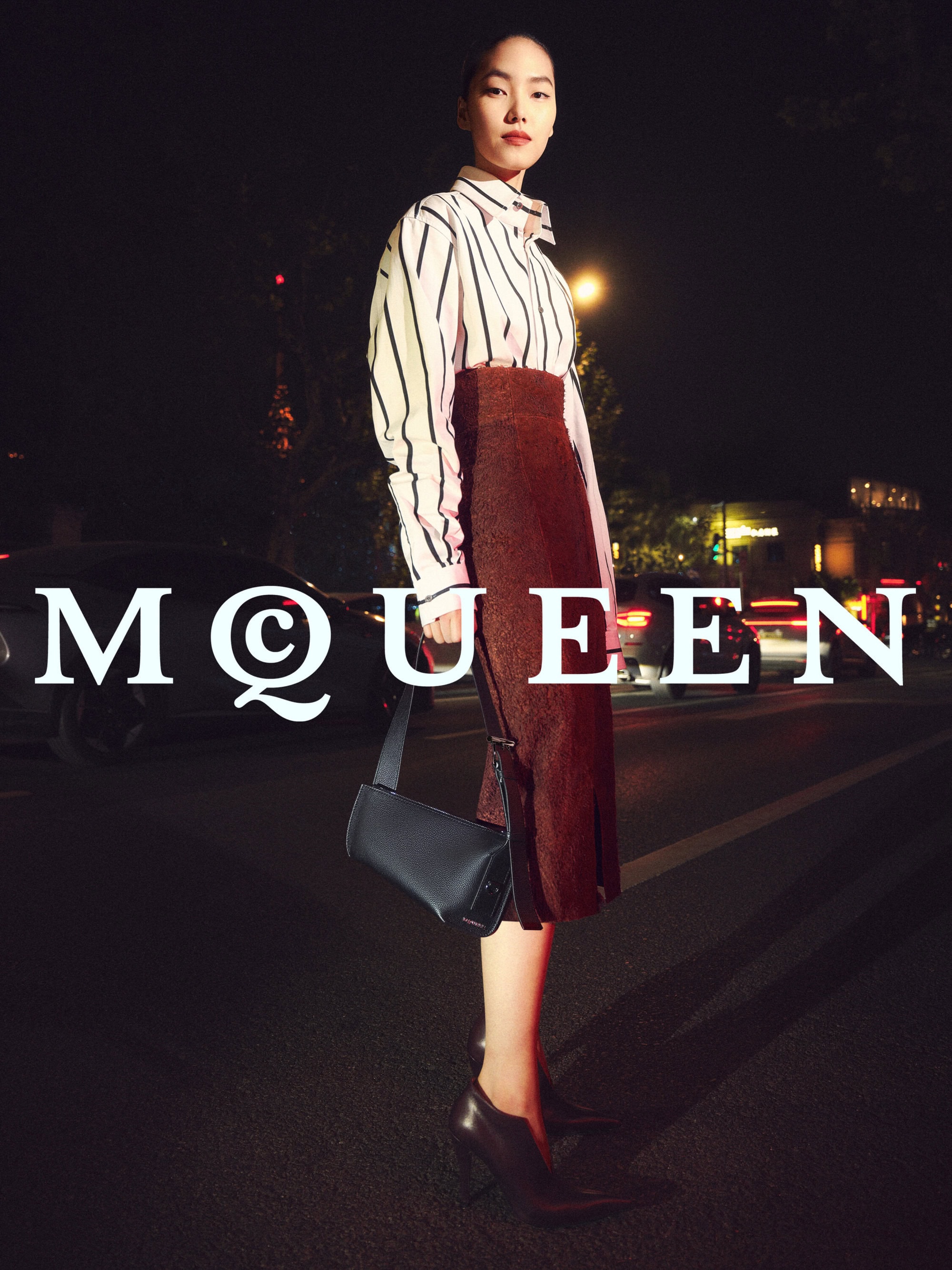 Model Zhang Youhao holding a black handbag on a city street at night for McQueen Lunar New Year campaign