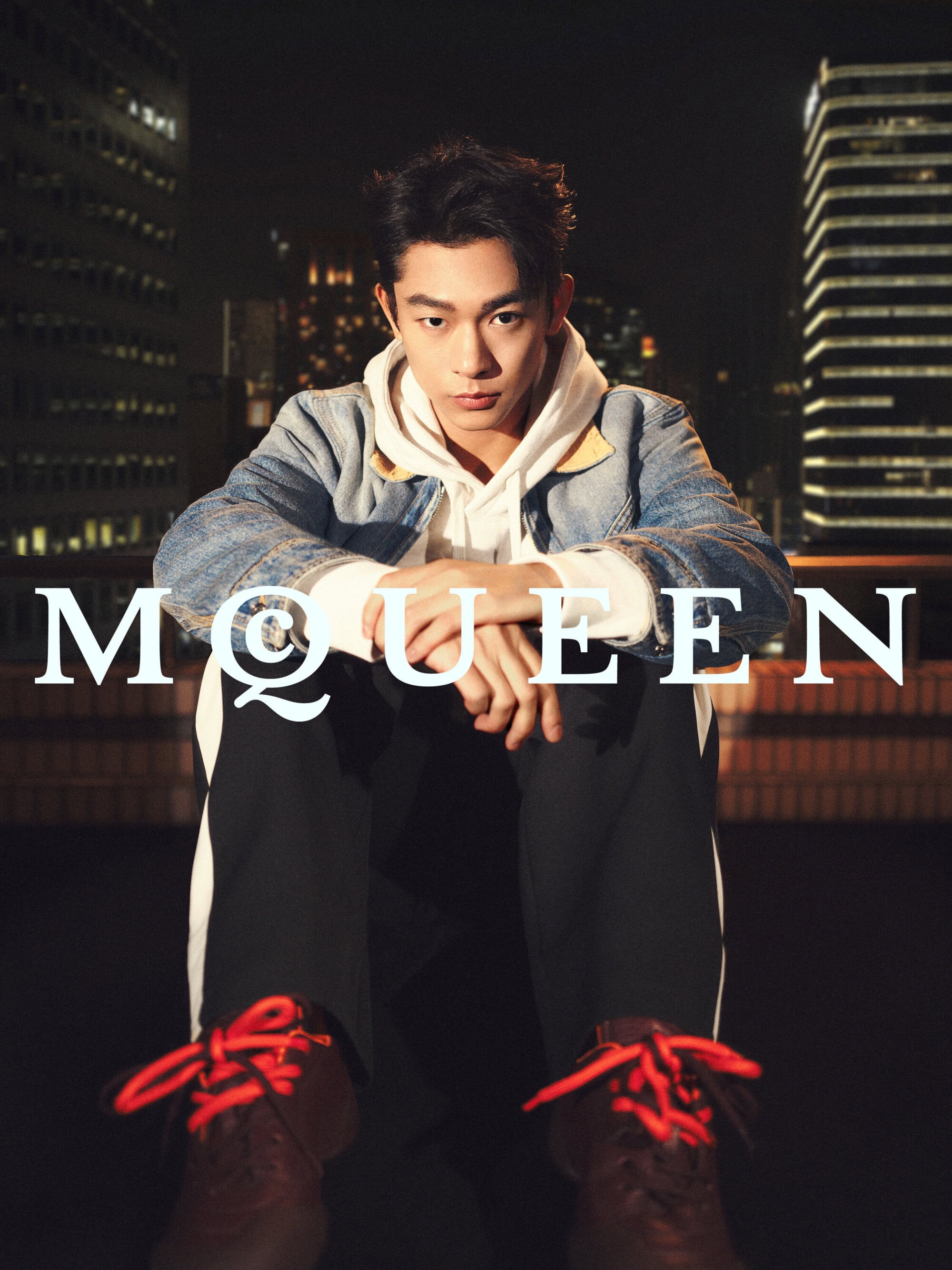Model Zhang Youhao seated outdoors at night wearing a denim jacket and white hoodie for McQueen Lunar New Year campaign.