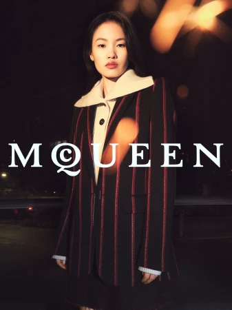 Model wearing a black and red striped blazer with a large white collar outdoors at night for a McQueen ad campaign.
