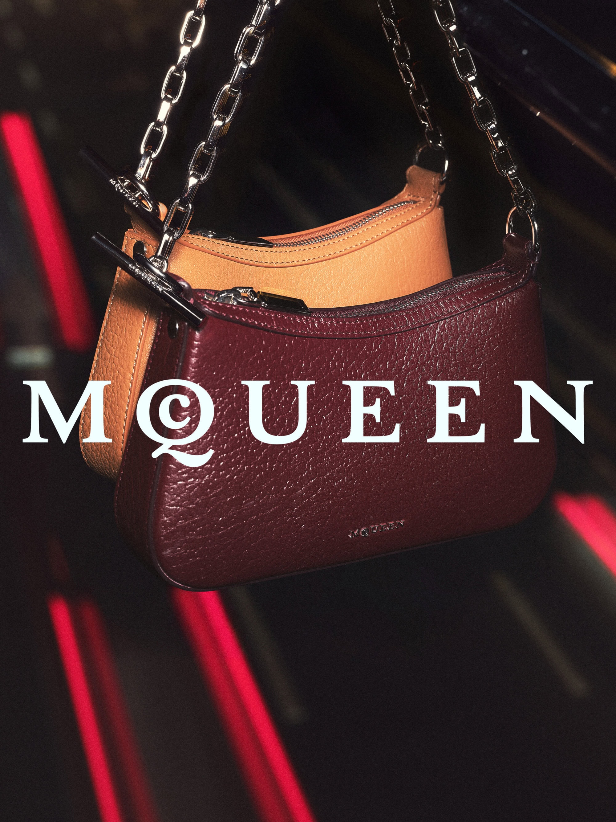 Two leather shoulder handbags with silver chain straps suspended against a dark red and black background