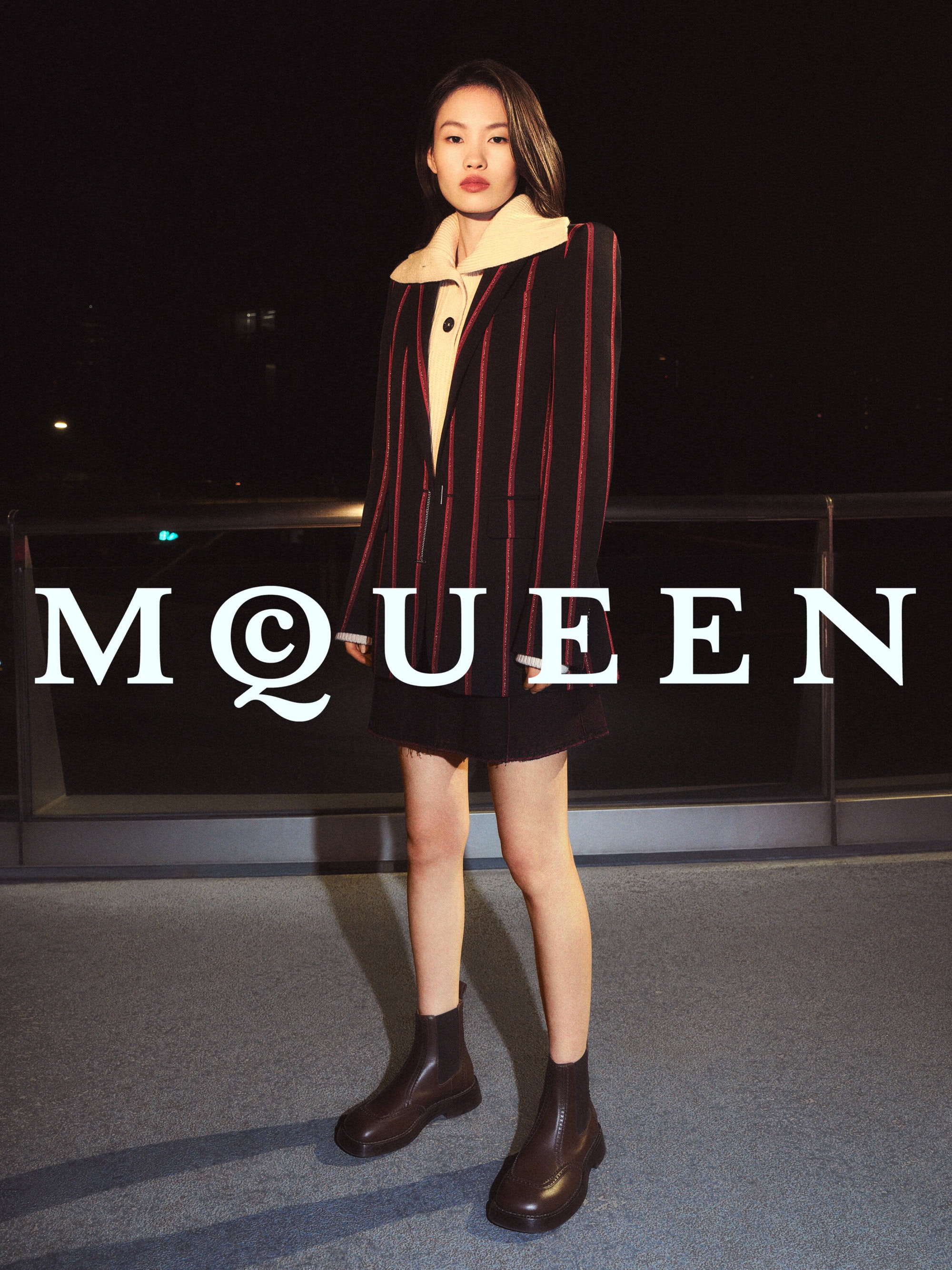 Model wearing striped blazer and dark skirt standing on rooftop at night for McQueen campaign