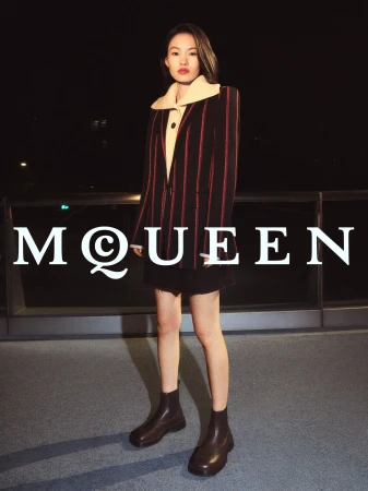 Model wearing striped blazer and dark skirt standing on rooftop at night for McQueen campaign
