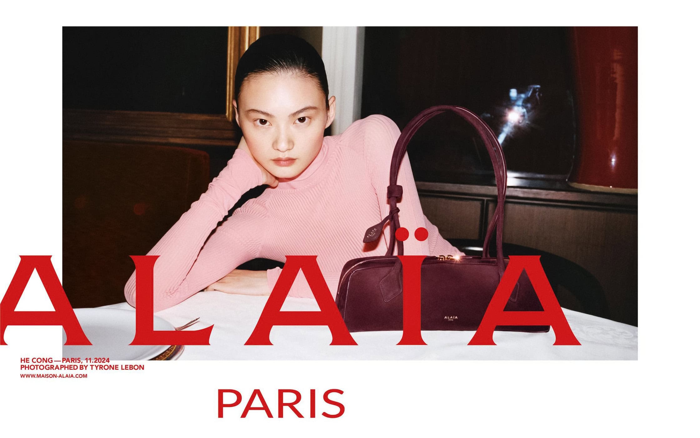 Model He Cong wearing a pink turtleneck sweater beside a burgundy leather handbag for Alaïa Lunar New Year campaign