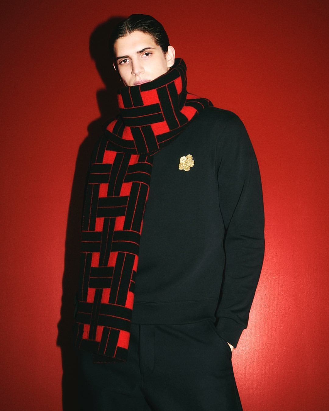 Model wearing a black sweater and red patterned scarf against a red background for Kenzo