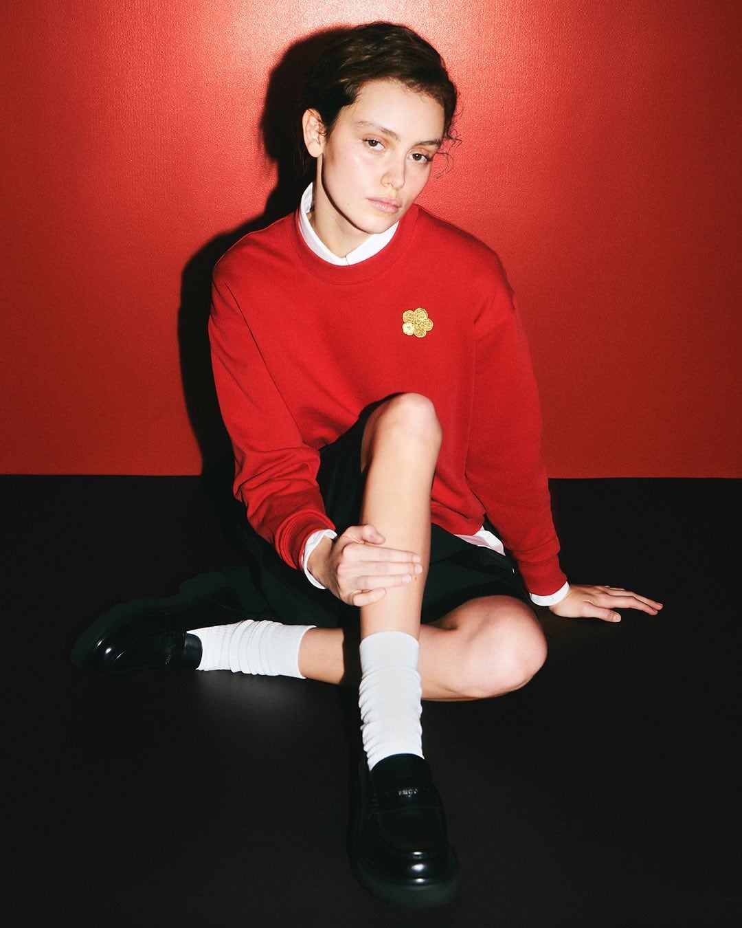 Model wearing a red sweatshirt and white socks seated against a vibrant red backdrop for Kenzo
