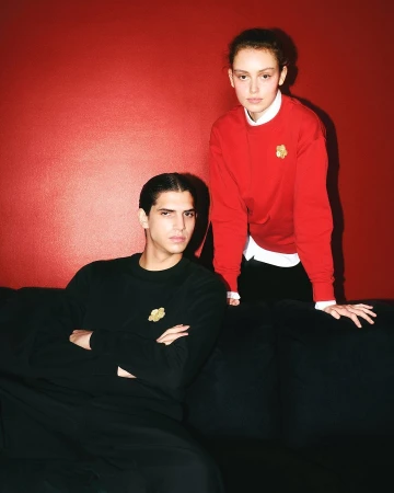 Two models posing against a vibrant red wall with a black sofa in Kenzo's Lunar New Year 2025 campaign.
